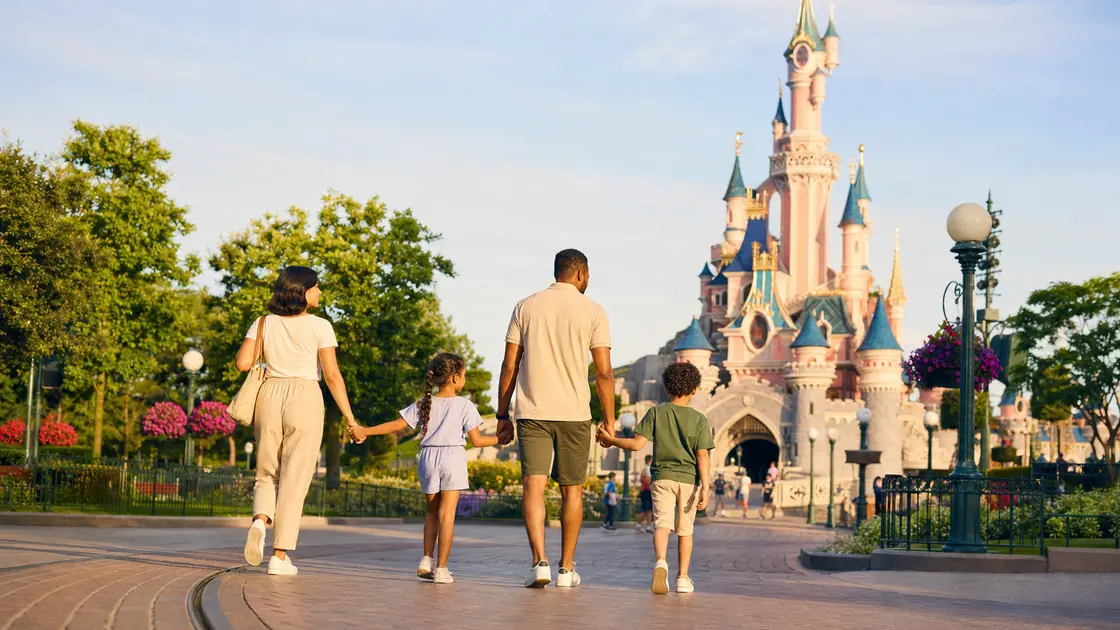 Une famille marche vers le château de Disneyland Paris dans un parc fleuri