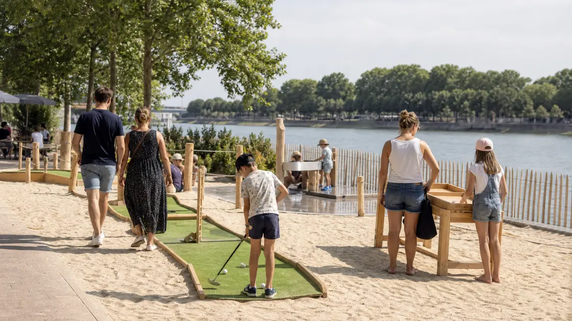 Des familles jouent au mini-golf sur une plage urbaine aménagée au bord d’un fleuve