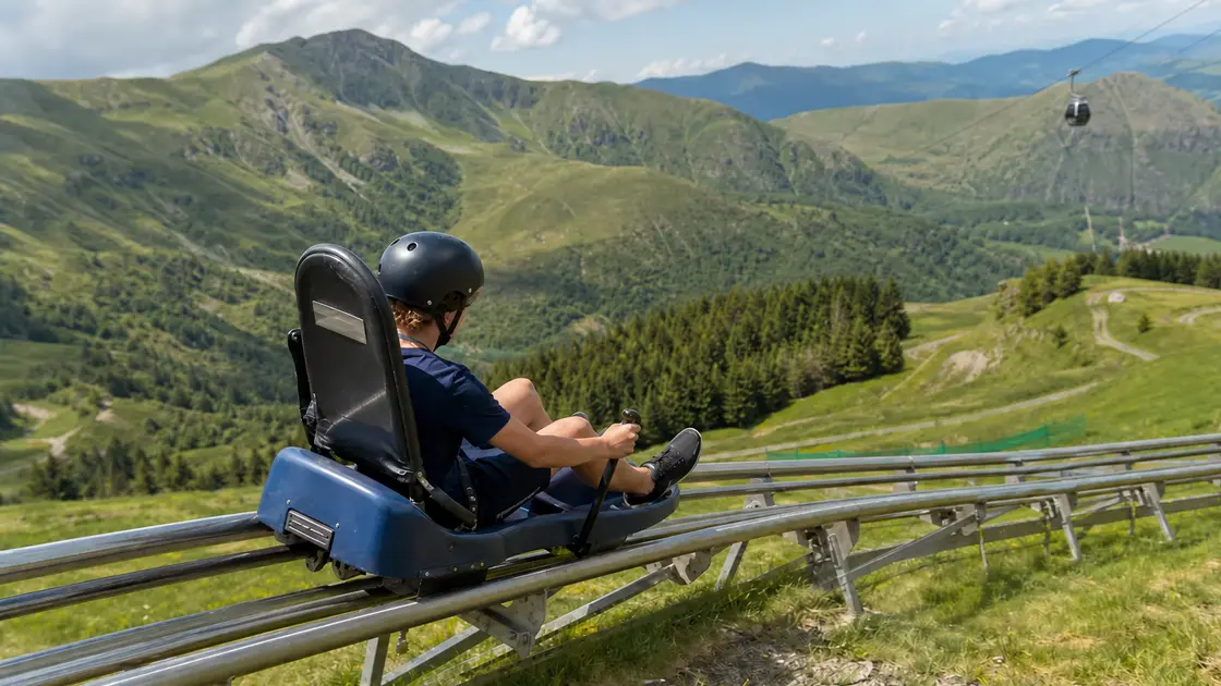 Un jeune descend une luge sur rails au Lioran avec les montagnes du Cantal en arrière-plan