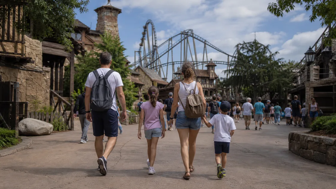 Une famille marche dans un parc d'attractions devant des montagnes russes