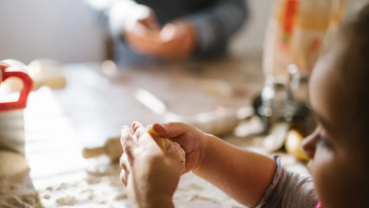 Enfant préparant une pâte sous le regard d'un adulte dans une cuisine