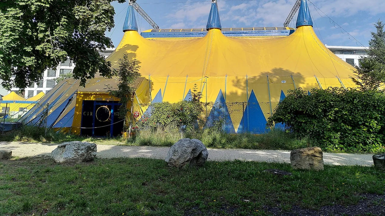 Chapiteau jaune et bleu à trois mâts entouré de verdure
