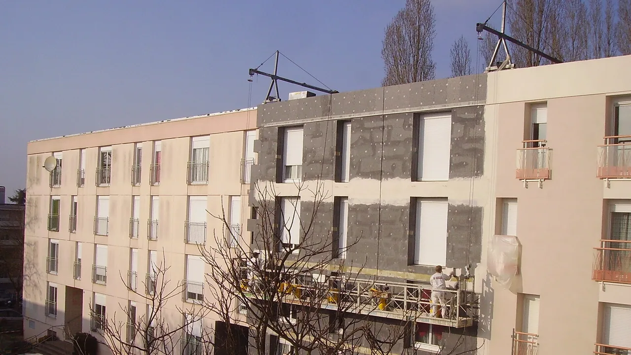 Ouvrier appliquant un enduit sur des panneaux d’isolation thermique extérieure d’un immeuble d’habitation