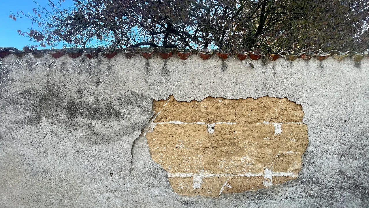 Fissures et détachement du revêtement extérieur d'un mur en pisé, photographié en France hors Dordogne